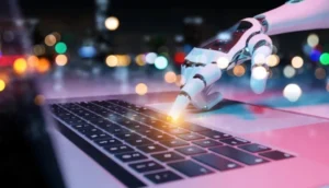 A robotic hand types on a laptop keyboard with glowing lights in the background