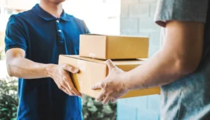 A delivery person hands two cardboard packages to a customer at their doorstep