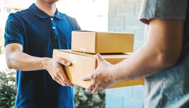 A delivery person hands two cardboard packages to a customer at their doorstep