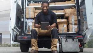 A delivery worker sits on the edge of an open van filled with packages