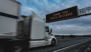 A white truck drives under a highway sign that reads "THANK YOU TRUCK DRIVERS"