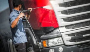 Man using a high-pressure hose to clean the front of a red HGV truck