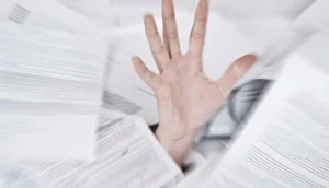 Hand reaching up through a chaotic flurry of flying paperwork