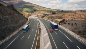 A wide open highway with a truck, car, and bus driving through a mountainous rural landscape