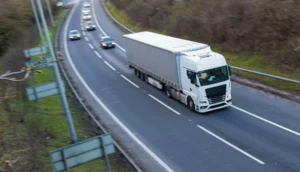 A white cargo truck drives on a mostly empty highway alongside a few cars