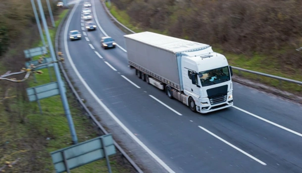 A white cargo truck drives on a mostly empty highway alongside a few cars
