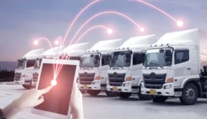 Person using a tablet to manage a fleet of white cargo trucks, with digital network lines connecting to each vehicle