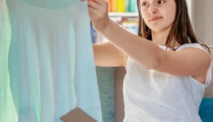Young woman examining a light blue dress at home with a skeptical expression