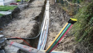 A trench with exposed multi-colored fiber optic cables being laid underground